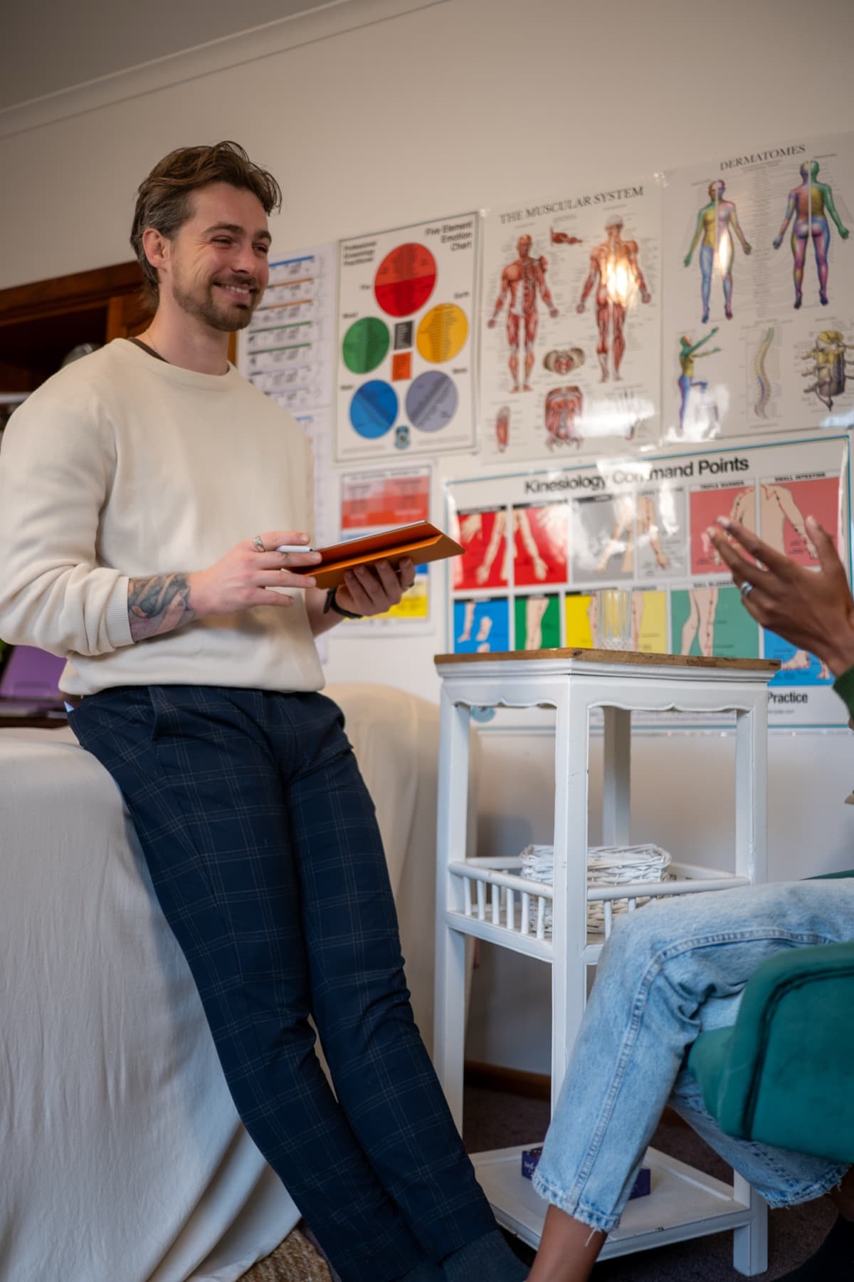 Vildan leaning on the treatment table, smiling as he talks with a client