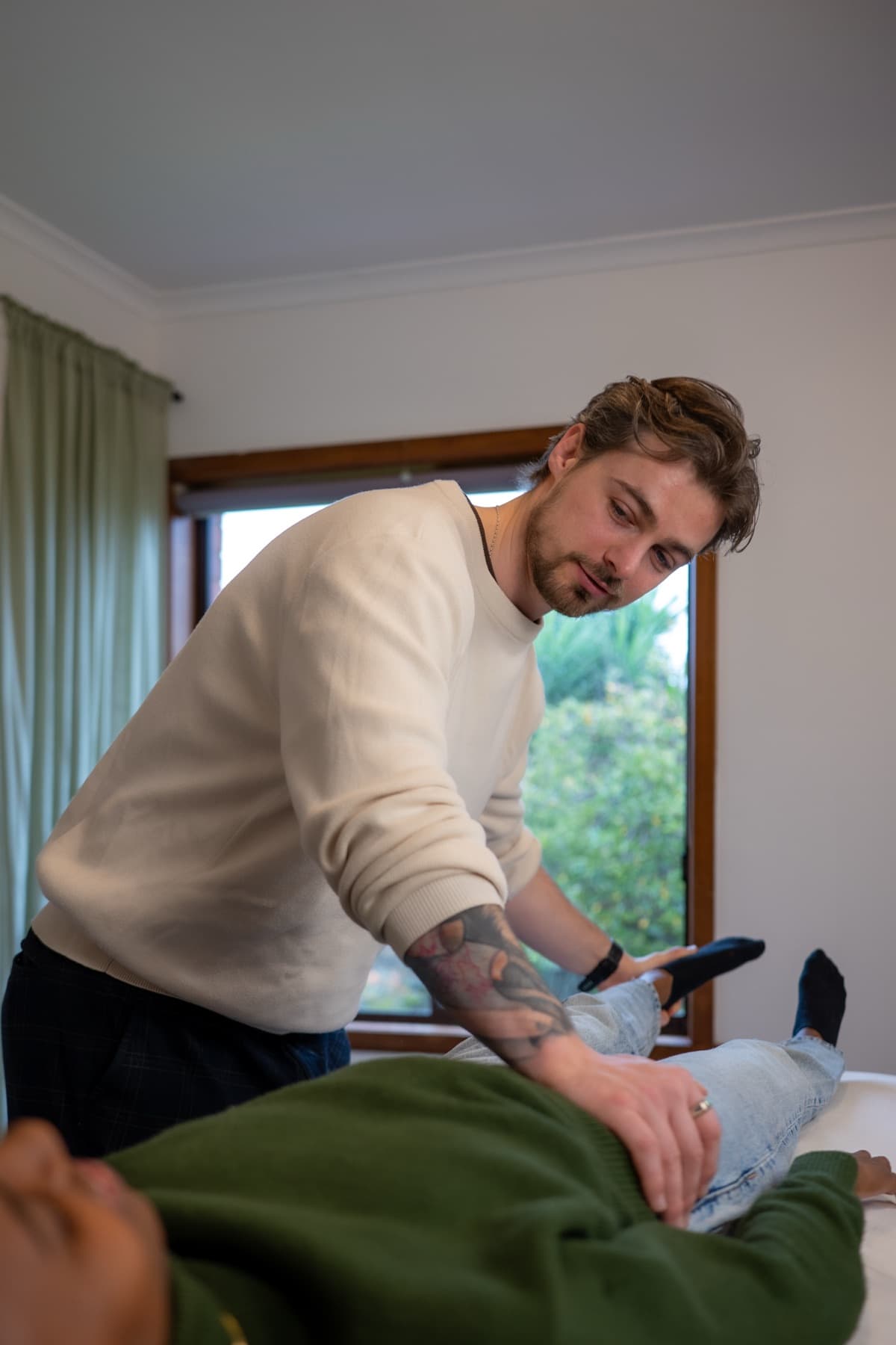 Vildan Alihodzic leans over the treatment table, one hand on the client's hip and one at her lower leg, during muscle monitoring in Moorabbin.